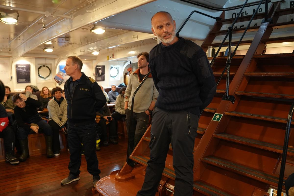 en mann i st&aring;r ved en trapp og snakker itil en gruppe mennesker